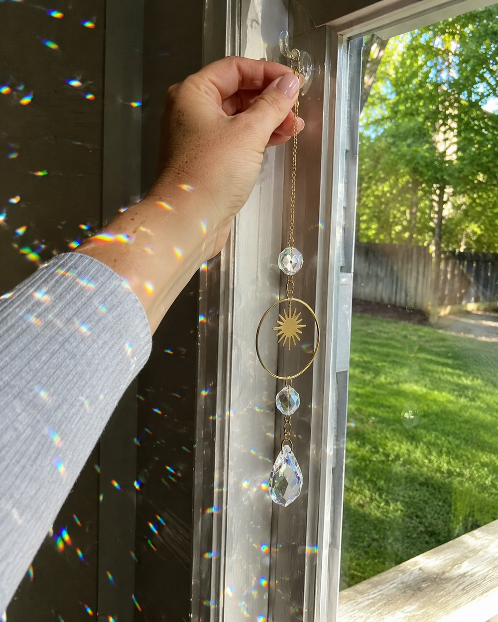 Hand hanging crystal suncatcher beside a sunny window