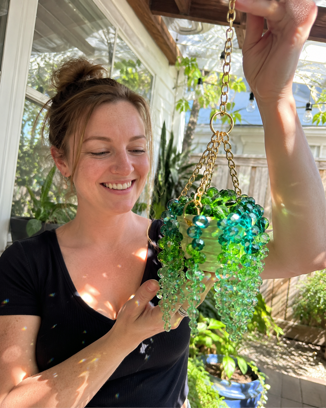 Woman holding green beaded hanging plant suncatcher on sunny patio