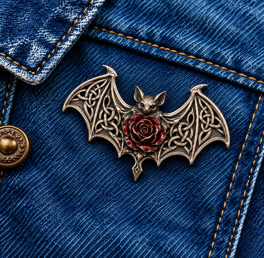 Gothic bat brooch with ornate wings and a deep red rose center on denim